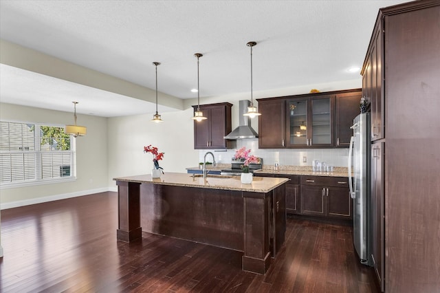 kitchen featuring dark brown cabinetry, pendant lighting, wall chimney exhaust hood, dark hardwood / wood-style floors, and light stone countertops