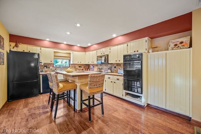 kitchen with decorative backsplash, a kitchen island, light hardwood / wood-style flooring, black appliances, and a kitchen bar