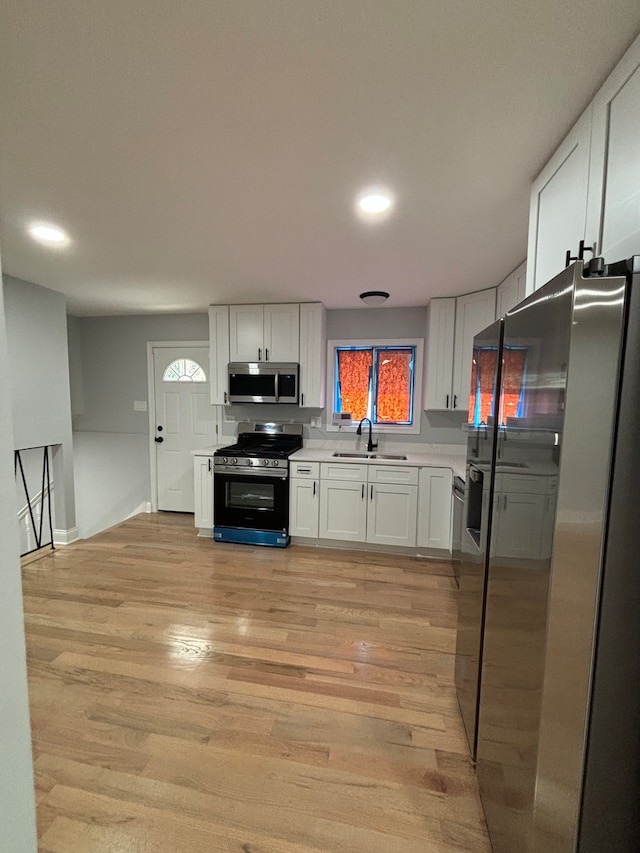 kitchen featuring white cabinets, stainless steel appliances, sink, and light hardwood / wood-style flooring