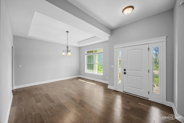 foyer featuring dark wood-type flooring, a raised ceiling, and a chandelier