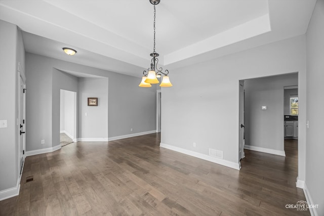 unfurnished room with a notable chandelier, a raised ceiling, and dark hardwood / wood-style flooring