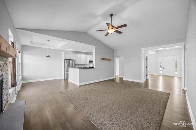 unfurnished living room with lofted ceiling, ceiling fan, a stone fireplace, and dark hardwood / wood-style flooring