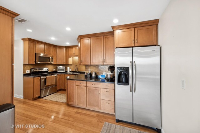 kitchen featuring backsplash, sink, dark stone countertops, appliances with stainless steel finishes, and light hardwood / wood-style floors