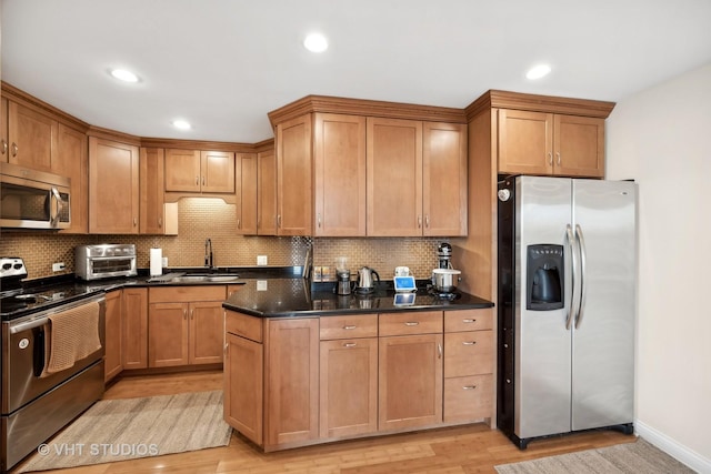 kitchen featuring tasteful backsplash, dark stone counters, stainless steel appliances, sink, and light hardwood / wood-style floors