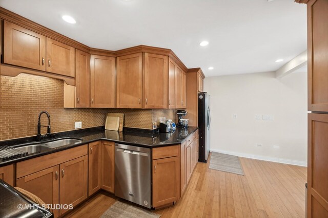 kitchen featuring sink, backsplash, dark stone counters, appliances with stainless steel finishes, and light wood-type flooring