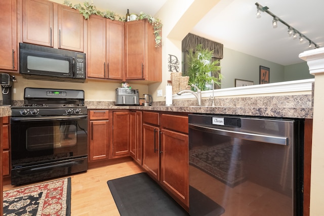 kitchen with rail lighting, sink, black appliances, stone counters, and light hardwood / wood-style floors