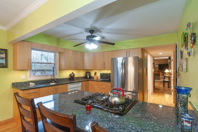 kitchen featuring sink, stainless steel appliances, crown molding, dark stone counters, and light wood-type flooring