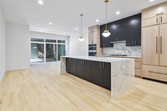 kitchen with light brown cabinetry, decorative light fixtures, and a kitchen island with sink