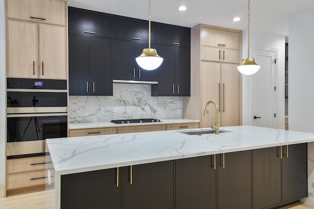 kitchen featuring sink, light brown cabinetry, decorative light fixtures, and a center island with sink