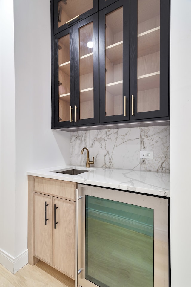 bar with light brown cabinets, backsplash, wine cooler, sink, and light wood-type flooring