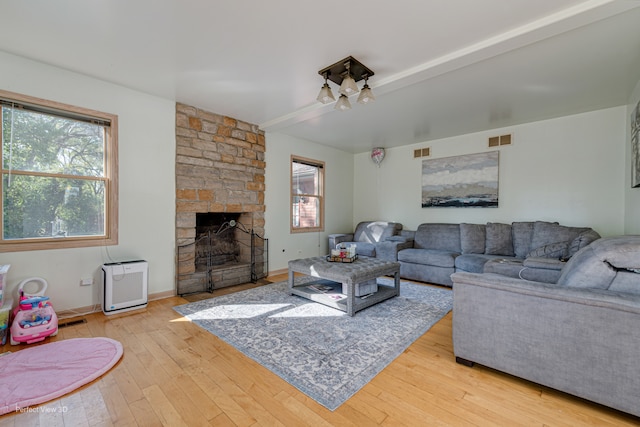 living room with light wood-type flooring, a wealth of natural light, and a stone fireplace