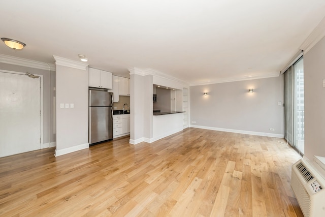 unfurnished living room with light hardwood / wood-style floors, ornamental molding, a wealth of natural light, and a wall mounted AC