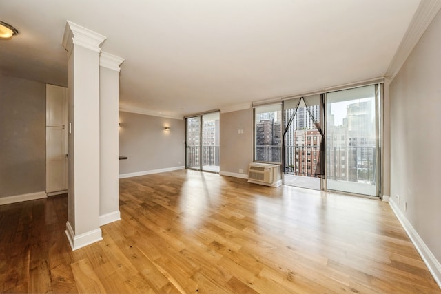 unfurnished living room featuring light hardwood / wood-style floors, ornamental molding, a wall unit AC, and ornate columns