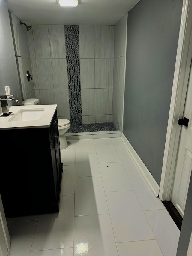 bathroom with vanity, toilet, a tile shower, tile walls, and tile patterned flooring