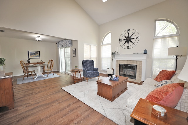 living room with plenty of natural light, high vaulted ceiling, light wood-type flooring, and a tile fireplace