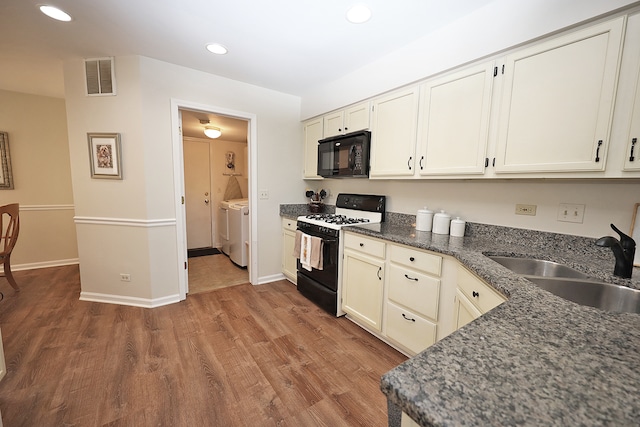 kitchen with black appliances, wood-type flooring, sink, dark stone counters, and washer and dryer