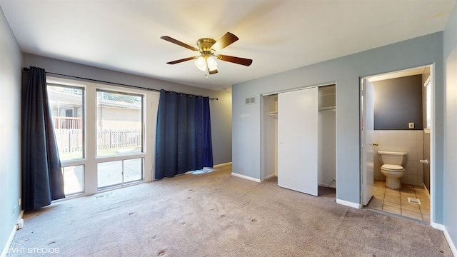 unfurnished bedroom with light carpet, ensuite bath, ceiling fan, and tile walls