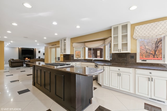 kitchen featuring tasteful backsplash, dark stone counters, light tile patterned flooring, stainless steel gas cooktop, and sink