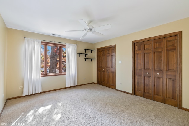 unfurnished bedroom featuring carpet, two closets, and ceiling fan