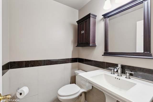 bathroom featuring toilet, sink, and tile walls