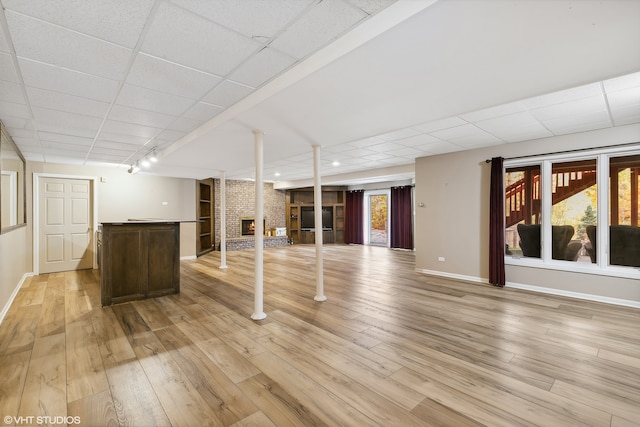 basement featuring a drop ceiling, light hardwood / wood-style flooring, and a fireplace