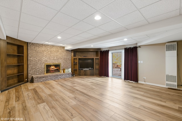 unfurnished living room with a drop ceiling, light wood-type flooring, and a brick fireplace