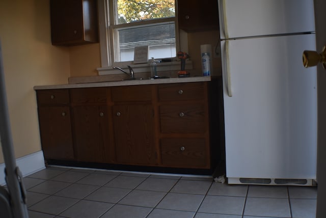 kitchen featuring light tile patterned flooring, dark brown cabinetry, white refrigerator, and sink