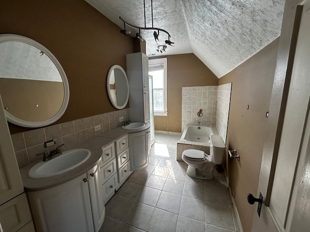 bathroom featuring lofted ceiling, vanity, tiled tub, toilet, and a textured ceiling