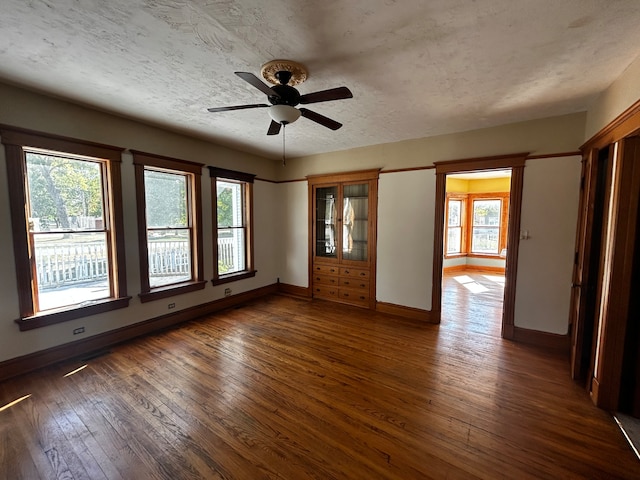 empty room with ceiling fan, plenty of natural light, and dark hardwood / wood-style floors