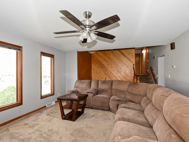 carpeted living room featuring ceiling fan and wooden walls