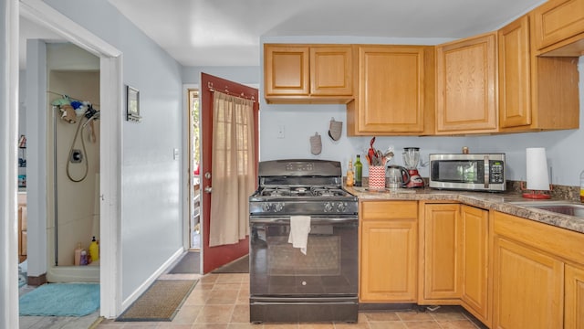 kitchen with light tile patterned flooring, sink, black gas range oven, and light brown cabinetry