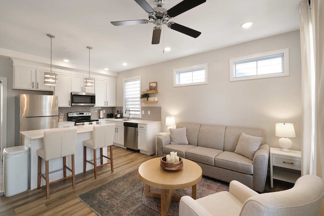 living room with light wood-type flooring, ceiling fan, and sink