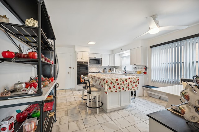 kitchen featuring tasteful backsplash, black double oven, a kitchen island, ceiling fan, and white cabinetry