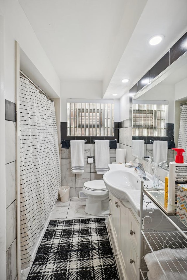 bathroom featuring walk in shower, vanity, toilet, and tile walls