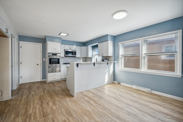 kitchen with kitchen peninsula, a kitchen breakfast bar, stainless steel appliances, light hardwood / wood-style flooring, and white cabinets