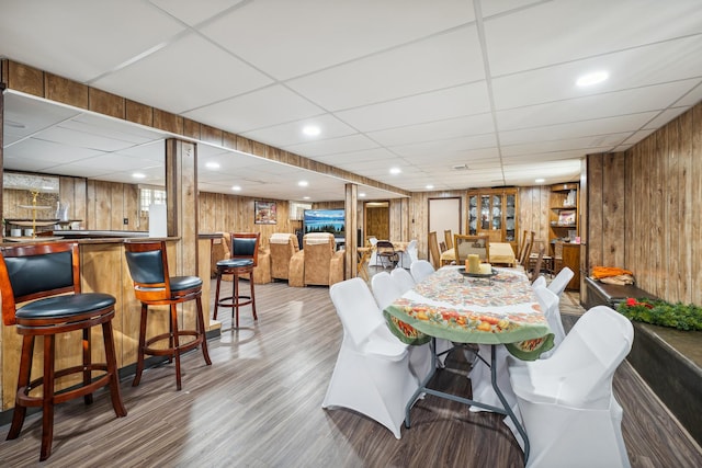 dining area featuring a paneled ceiling, wood walls, light hardwood / wood-style floors, and indoor bar