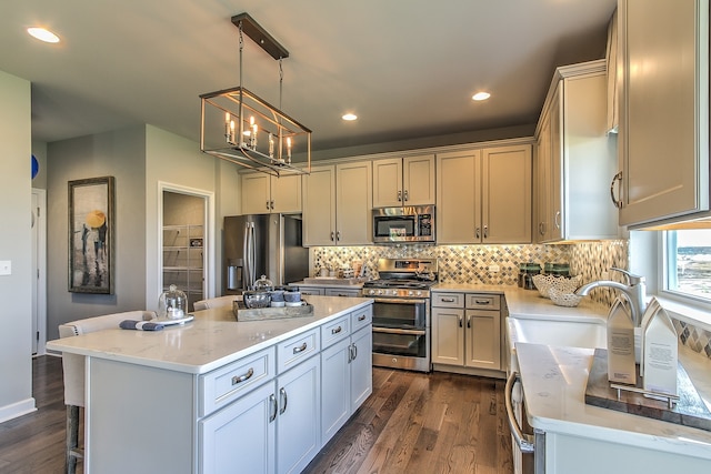 kitchen with light stone countertops, a center island, dark wood-type flooring, sink, and appliances with stainless steel finishes