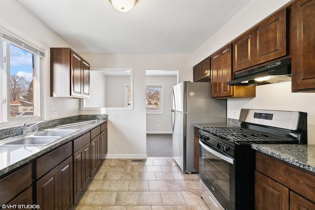 kitchen with dark brown cabinetry, sink, dark stone counters, light carpet, and appliances with stainless steel finishes