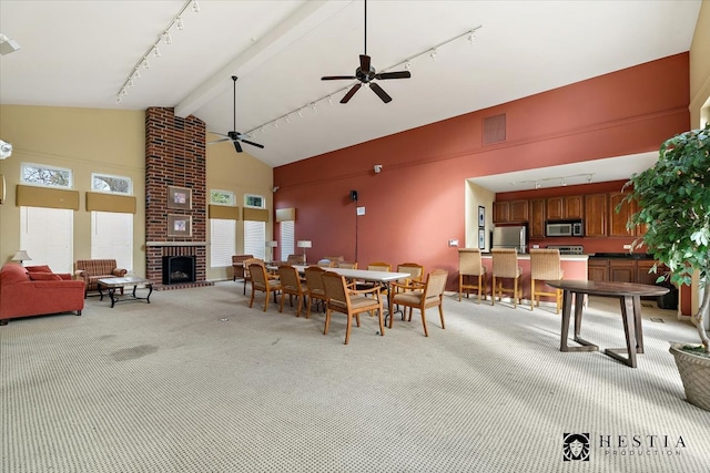 carpeted dining area with beam ceiling, track lighting, ceiling fan, high vaulted ceiling, and a fireplace