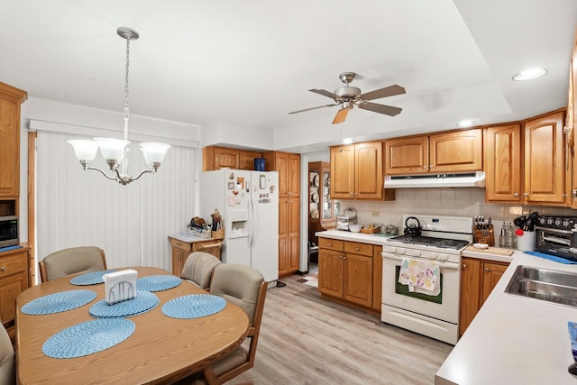 kitchen featuring hanging light fixtures, white appliances, light wood-type flooring, ceiling fan with notable chandelier, and tasteful backsplash