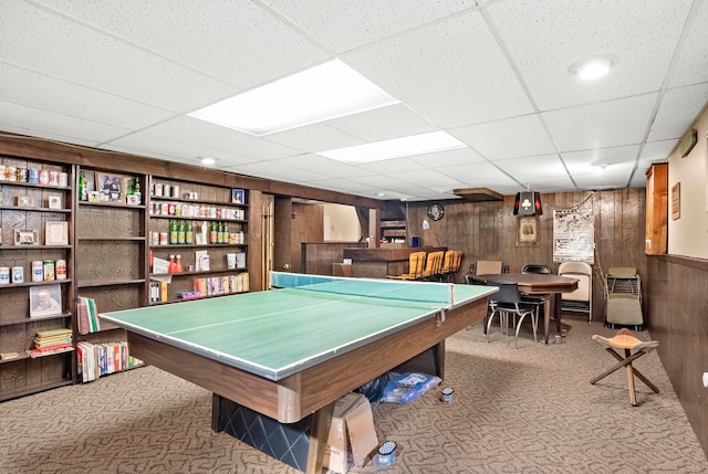 recreation room with a drop ceiling, wood walls, light colored carpet, and bar area