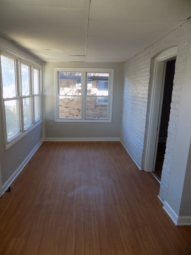 spare room featuring a healthy amount of sunlight, dark hardwood / wood-style floors, and brick wall