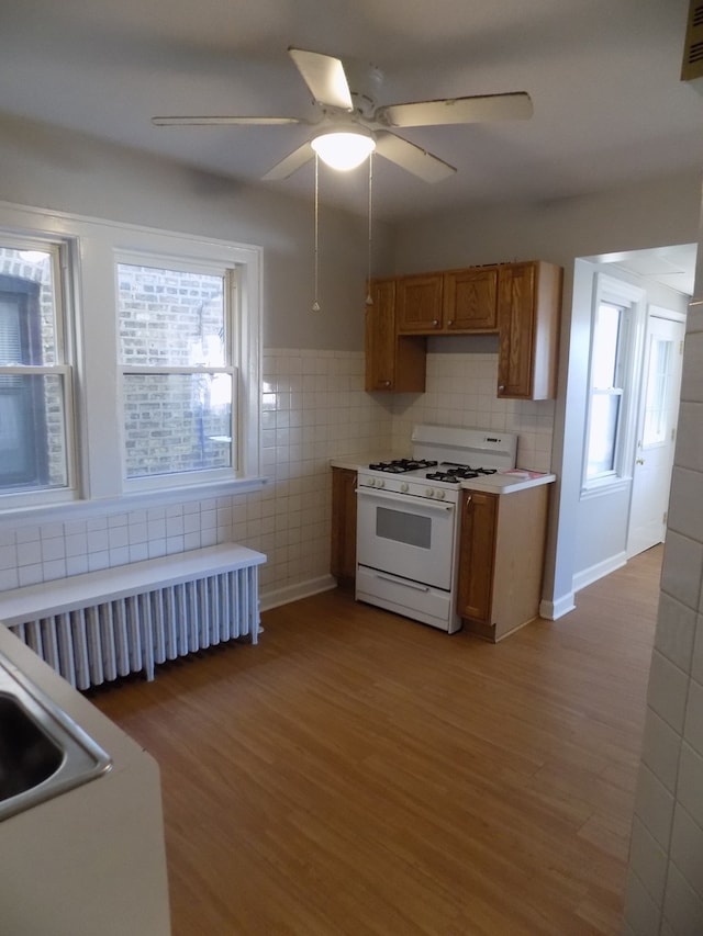 kitchen with white gas range oven, radiator, tile walls, and light hardwood / wood-style flooring