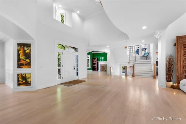 entrance foyer with a towering ceiling, crown molding, and light hardwood / wood-style flooring