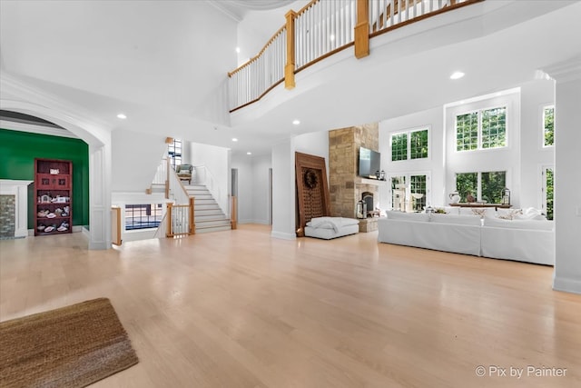 unfurnished living room featuring a stone fireplace, light hardwood / wood-style flooring, a towering ceiling, and a healthy amount of sunlight