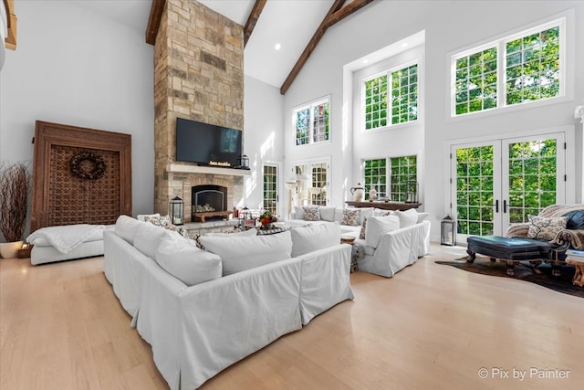 living room with beam ceiling, french doors, a stone fireplace, light hardwood / wood-style flooring, and high vaulted ceiling