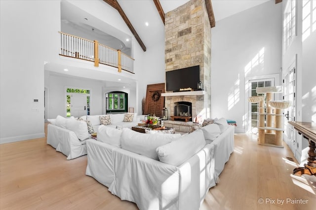 living room with a fireplace, high vaulted ceiling, beam ceiling, and light hardwood / wood-style flooring