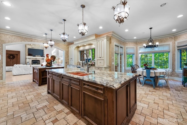 kitchen with ornamental molding, decorative light fixtures, sink, and a kitchen island with sink