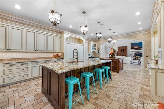 kitchen with decorative backsplash, cream cabinets, hanging light fixtures, a breakfast bar area, and a center island with sink