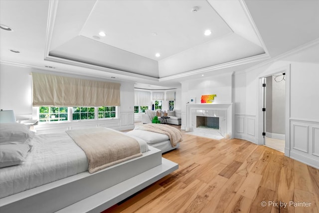 bedroom featuring a high end fireplace, crown molding, hardwood / wood-style floors, and a raised ceiling